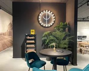 Moderne kantoorruimte met verlichte wandklok, grijze muur, groene planten, ronde tafel en blauwe stoelen voor ontmoetingen en brai