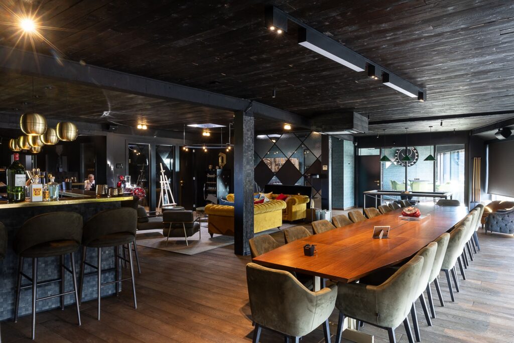 Modern bedrijfsruimte met houten tafel, gele fauteuils, bar en lounge-gedeelte met professionele verlichting