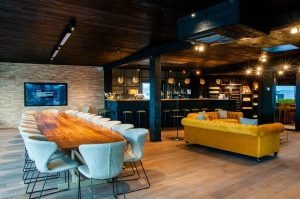Modern kantoorruimte met gele loungezitplaats, houten vloer, verlichte boekenkasten en werktafels met blauwe schermen