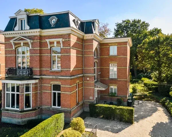 Elegant bakstenen herenhuis met mansardedak, grote ramen en groene tuinen, representatief voor vastgoedportfolio's